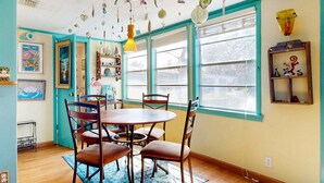 Comedor con una mesa redonda, cuatro sillas, un tapete azul y una ventana con persianas.