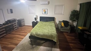 Ein Schlafzimmer mit Bett, Schreibtisch, Stuhl, Pflanze und Deckenventilator.