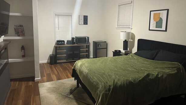Ein Schlafzimmer mit Bett, Schreibtisch, Computer, Stuhl, Lampe und Deckenventilator.