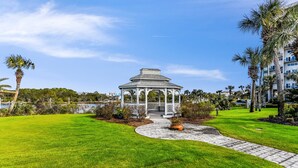 Un mirador con techo blanco y columnas, rodeado de un césped cuidado y palmeras.