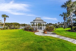 A gazebo with a white roof and columns, surrounded by a well-maintained lawn and palm trees. - Waterfront 2BR condo in Panama City Beach, perfect for a relaxing getaway. (Panama City Beach)