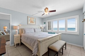 Ein Schlafzimmer mit Bett, Nachttischen, einer Bank, einem Deckenventilator und einem Fenster mit Jalousien.