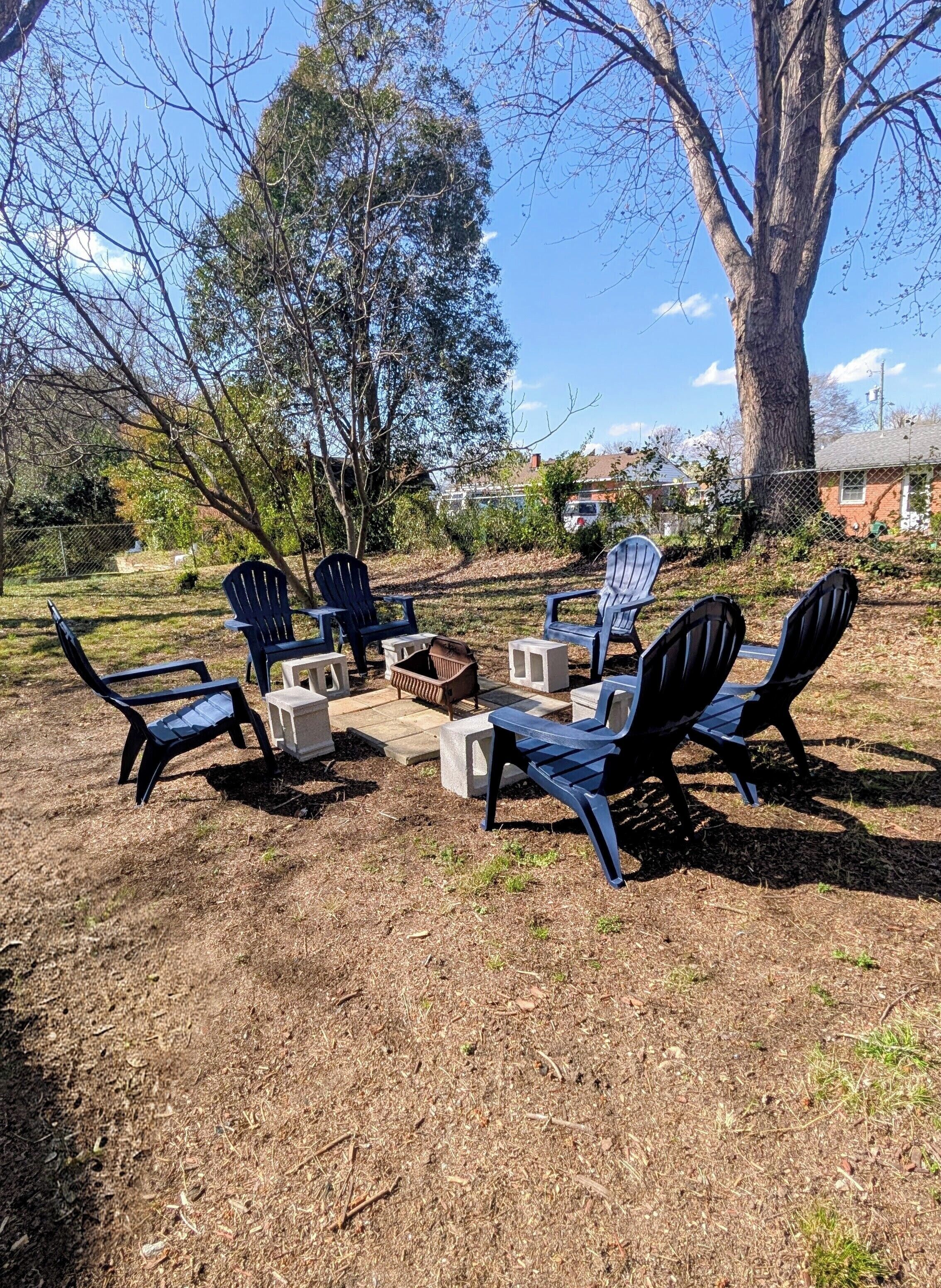 Un patio trasero con sillas Adirondack, una chimenea y un árbol grande.