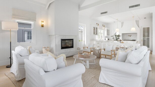 A spacious living room with white furniture, a fireplace, and a kitchen area. - The Homestead at Farmhouse Hunter Valley (Pokolbin)