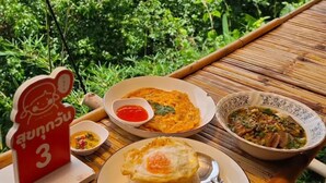 A table with food, a red sign, and a view of greenery. - Phuthiptara Resort (Khlung)