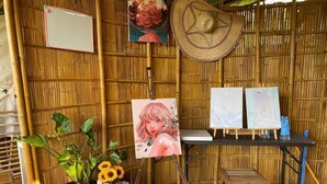A room with bamboo walls, a painting of a woman, and a table with a colorful striped tablecloth. - Phuthiptara Resort (Khlung)
