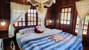 A room with a bed, a chair, a hanging light fixture, and windows. - Phuthiptara Resort (Khlung)