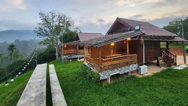 A rustic lodge with a wooden deck and a covered area, surrounded by lush greenery and a mountainous backdrop. - Phuthiptara Resort (Khlung)