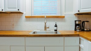 A kitchen with white cabinets, a stainless steel sink, a coffee maker, and a window with blinds. - Charming 1Br With French Door Home Theater Screen & Rain Shower (Philadelphia)