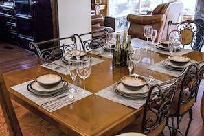 A dining table set with plates, glasses, and bottles, surrounded by chairs with ornate metalwork. - Villa de La Rosa en Valle de Gpe  (Valle de Guadalupe)