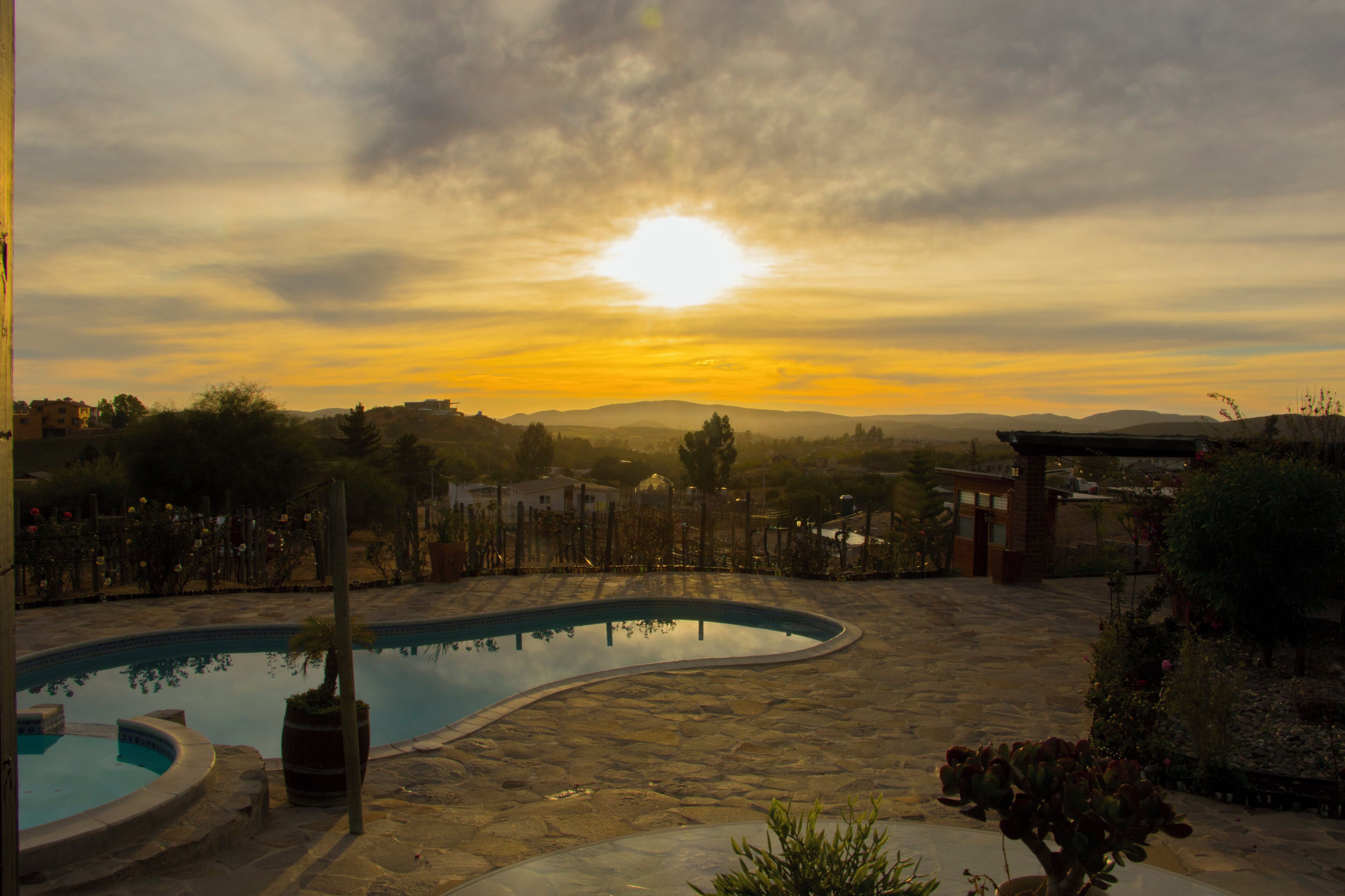 A swimming pool with a stone deck, surrounded by greenery and a view of distant hills.