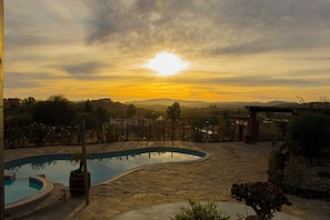 A swimming pool with a stone deck, surrounded by greenery and a view of distant hills. - Villa de La Rosa en Valle de Gpe  (Valle de Guadalupe)