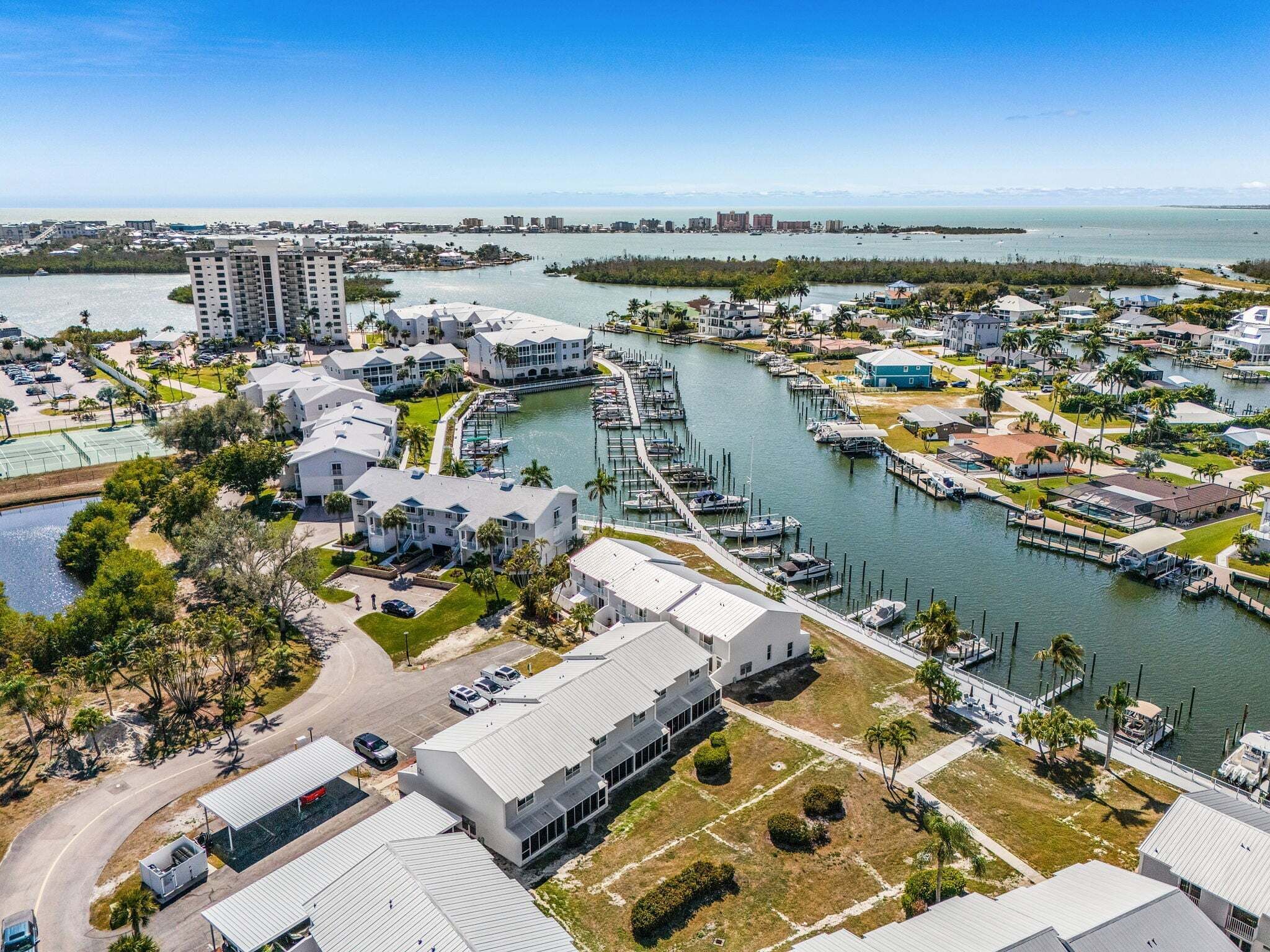 An aerial view of a marina with boats docked, a marina building, and surrounding residential buildings.