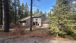 A modern two-story house with a garage, surrounded by a forested area. - 3-bedroom house in brilliant Black Butte ranch with cozy living spaces (Sisters)