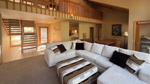 A spacious living area with a large sectional sofa, a wooden staircase, and a dining area. - 3-bedroom house in brilliant Black Butte ranch with cozy living spaces (Sisters)