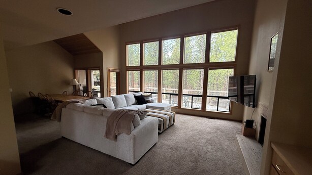 A spacious living area with a large sofa, a dining table, and a TV mounted on the wall. - 3-bedroom house in brilliant Black Butte ranch with cozy living spaces (Sisters)