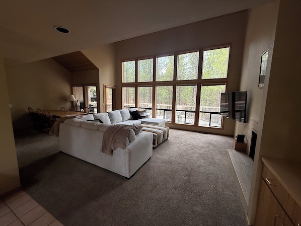 A spacious living area with a large sofa, a dining table, and a TV mounted on the wall.