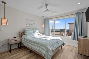 Een slaapkamer met een bed, nachtkastje, plafondventilator, raam met gordijnen en uitzicht.