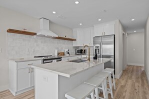 Een moderne keuken met witte kasten, een centraal eiland met barkrukken, een roestvrijstalen koelkast en een magnetron.