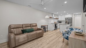 Un soggiorno moderno con divano in pelle, angolo pranzo con tavolo e sedie, cucina con pensili bianchi e ventilatore a soffitto.