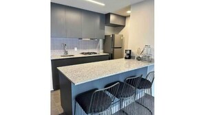 A modern kitchen with dark cabinets, a granite countertop, a gas stove, a refrigerator, and bar-style seating. - Cozy apartment in Americana 16 (Guadalajara)