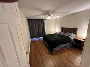 A bedroom with a bed, a nightstand, a ceiling fan, and a window with curtains. - 2BR/2BH Delightful Budget-Friendly Apt in Gnsville (Gainesville)