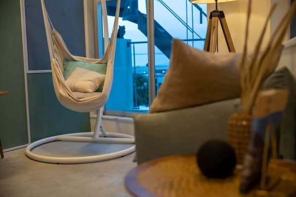Ein Zimmer mit Hängesessel, Sofa, Lampe und Blick auf ein Gebäude.