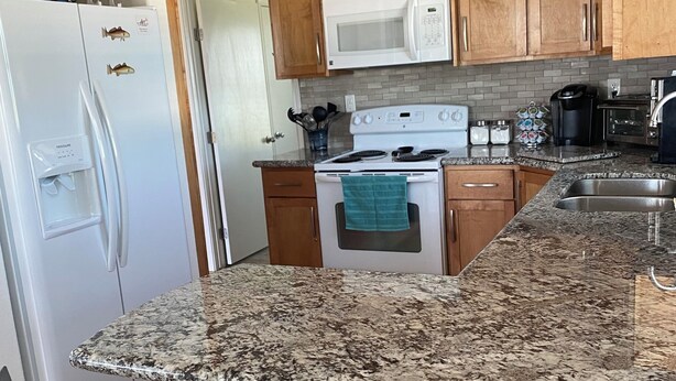 Una cocina con encimeras de granito, armarios de madera, un refrigerador blanco, una estufa y dos sillas.