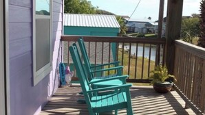 Una terraza de madera con tres mecedoras, una planta en maceta y vistas a un lago.