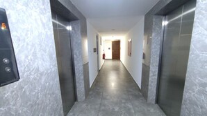 Un couloir aux murs et au sol en marbre, deux ascenseurs et une porte au bout.