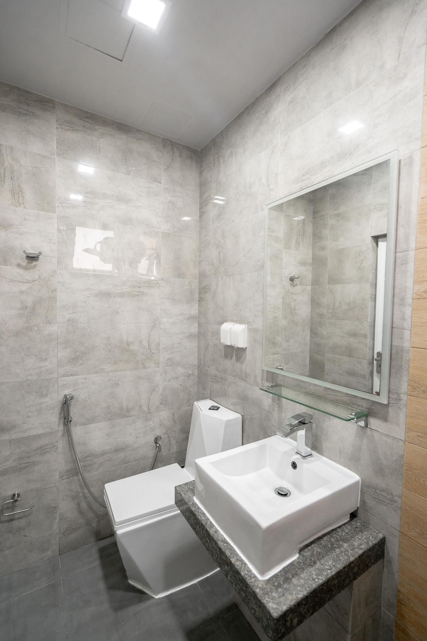 A modern bathroom with a glass shower enclosure, a white sink, and a marble-tiled shower wall.