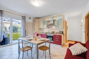 A modern kitchen with a dining area, a red sofa, and a balcony with curtains. - Agritur Laura - L'angolo dei Fiori 4 with Shared Garden, Torbole sul Garda, Italy (Torbole sul Garda)