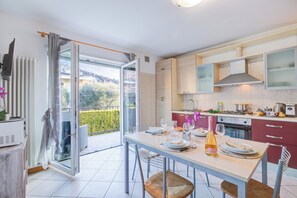 A modern kitchen with a dining area, a view of the outdoors, and a balcony with a sliding door. - Agritur Laura - L'angolo dei Fiori 4 with Shared Garden, Torbole sul Garda, Italy (Torbole sul Garda)
