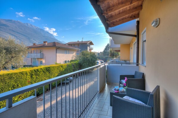 A balcony with a view of a mountain, a hedge, and a row of houses. - Agritur Laura - L'angolo dei Fiori 4 with Shared Garden, Torbole sul Garda, Italy (Torbole sul Garda)