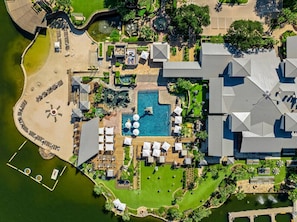 Ein Luftbild eines Resorts mit Schwimmbad, Liegestühlen und Strand.