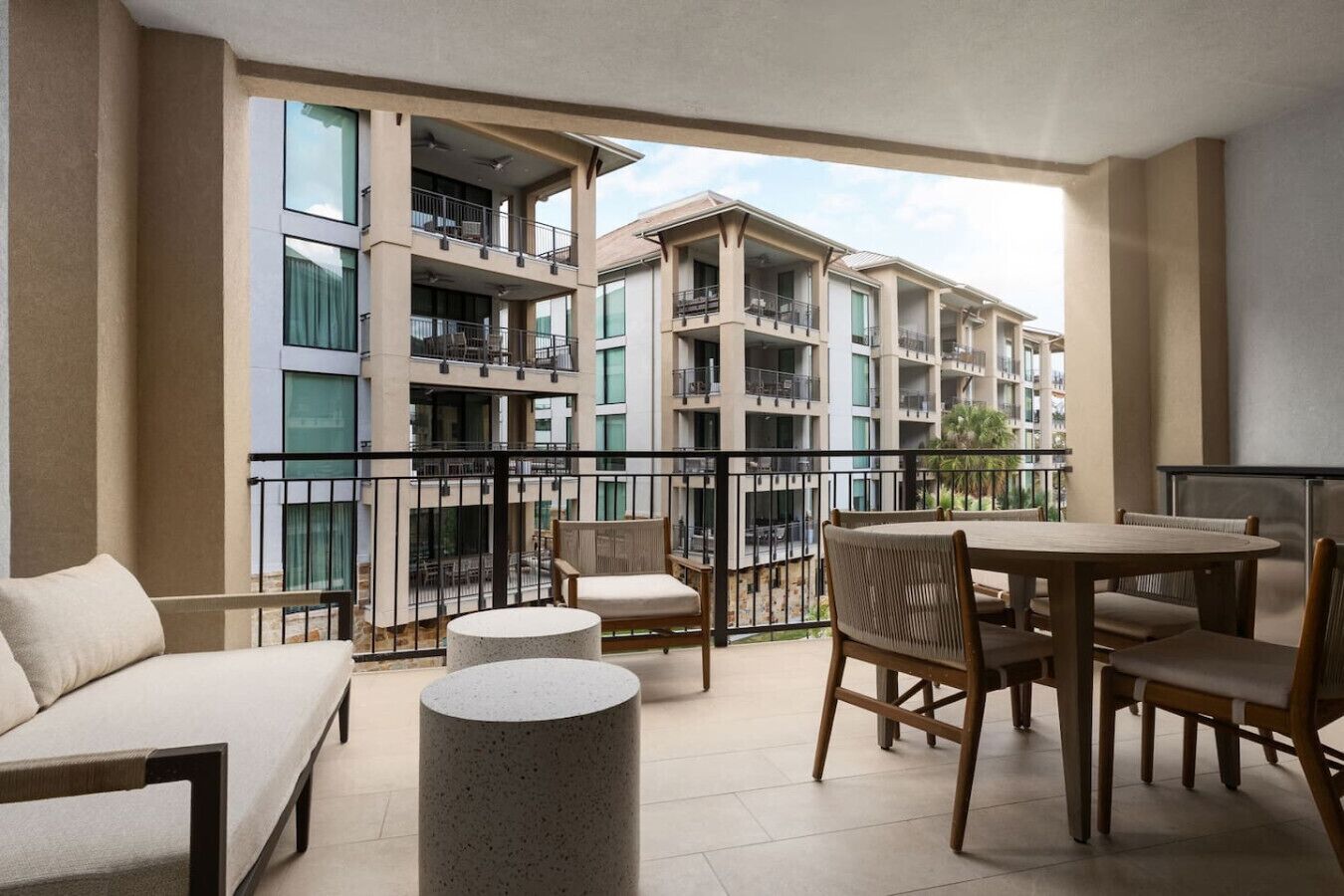 A balcony with a sofa, chairs, and a table, overlooking a multi-story building with balconies.