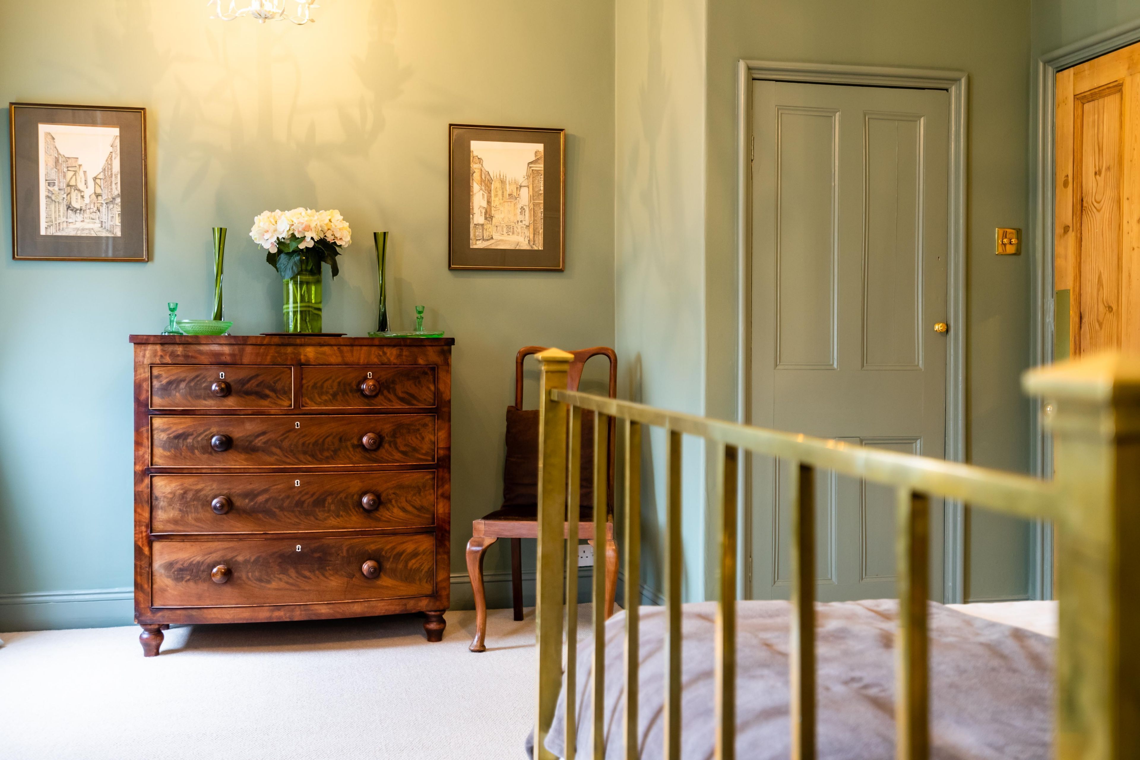 A bedroom with a wooden dresser, a chair, a door, and two framed pictures on the wall.