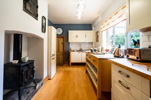 Una cocina con suelo de madera, armarios blancos, una estufa y una ventana con cortinas.