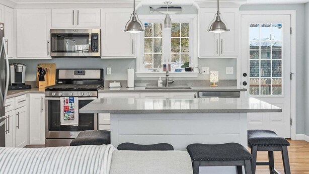 Una cocina moderna con armarios blancos, electrodomésticos de acero inoxidable, iluminación colgante y una isla grande con taburetes de bar.
