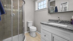 Un baño con cabina de ducha de vidrio, inodoro, lavamanos con encimera de granito y espejo sobre el lavamanos.