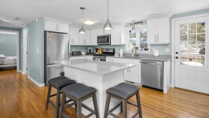 Una cocina moderna con armarios blancos, electrodomésticos de acero inoxidable y una isla central con taburetes de bar.