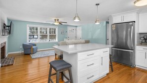 Una cocina con una isla central, armarios blancos, un refrigerador de acero inoxidable y un ventilador de techo.