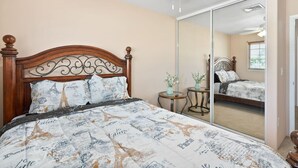 Een slaapkamer met een bed, een plafondventilator, een spiegel en een klein tafeltje met een vaas.