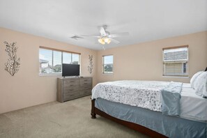 A bedroom with a bed, dresser, ceiling fan, and two windows.