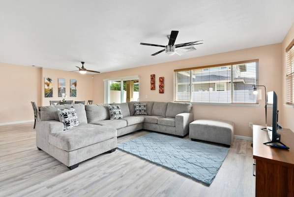A modern living room with a sectional sofa, a desk, and a ceiling fan.