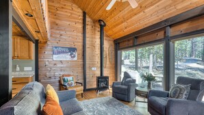 L’intérieur chaleureux d’un chalet avec une cheminée, des sièges confortables et de grandes fenêtres donnant sur la forêt.