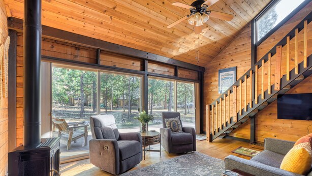 L’intérieur chaleureux d’un chalet avec une cheminée, des sièges confortables, de grandes fenêtres et un escalier en bois.