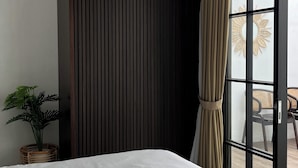Ein Hotelzimmer mit einem großen Bett, einer Topfpflanze, einem Fenster mit Vorhängen und Blick ins Freie.