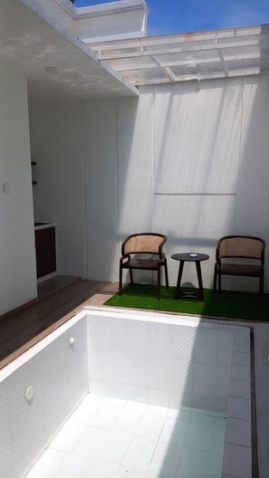 Ein kleiner, abgeschlossener Patio-Bereich mit zwei Korbstühlen und einem kleinen runden Tisch, weißen Wänden und einer geneigten Decke.
