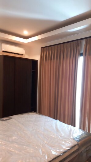 Ein Schlafzimmer mit einem Bett, einer Klimaanlage, einem Kleiderschrank und einem Fenster mit Vorhängen.